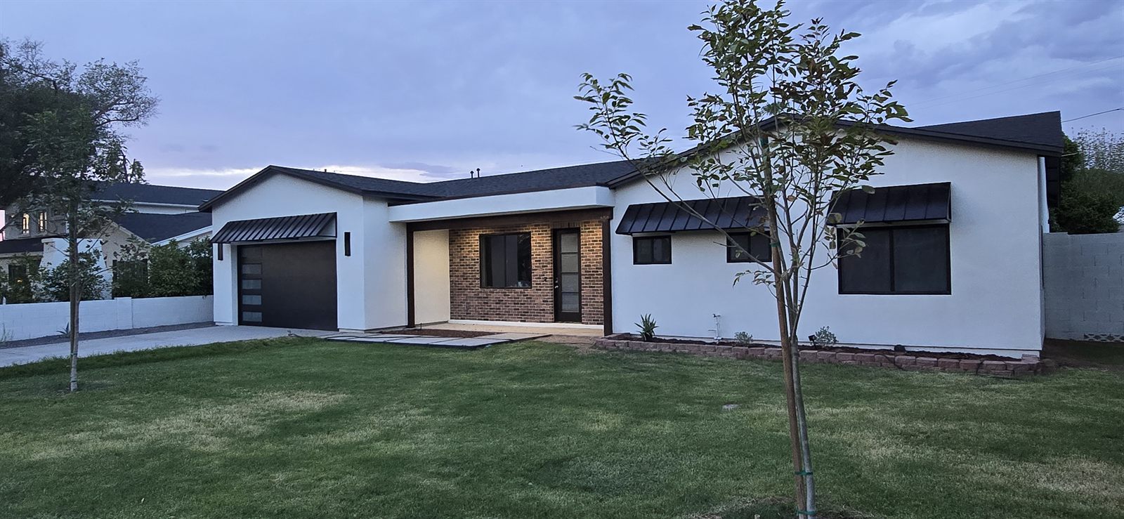 A Phoenix home transformed and expanded by SOKO Development, shown at dusk with new stucco, brick entry, and steel awnings