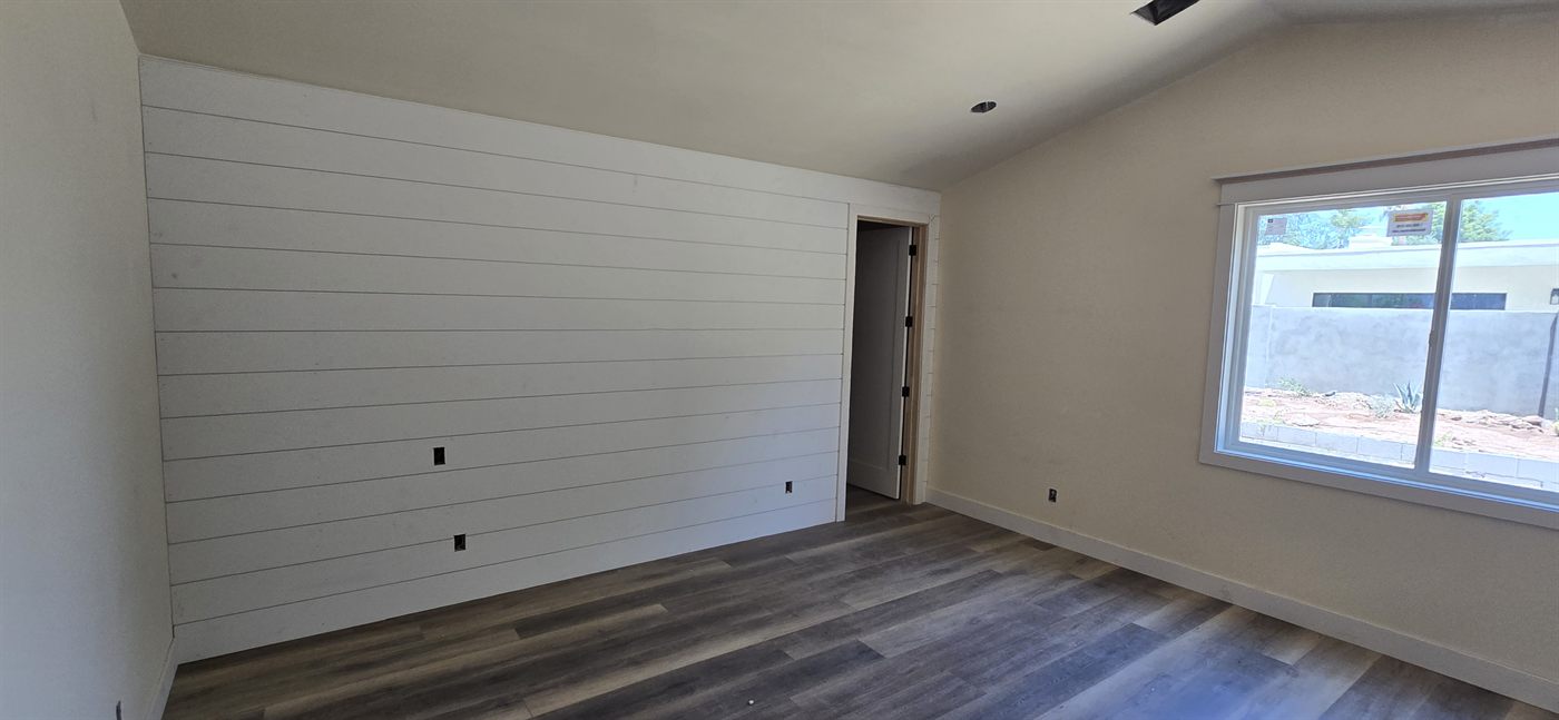 New primary bedroom with shiplap accent wall and vaulted ceiling